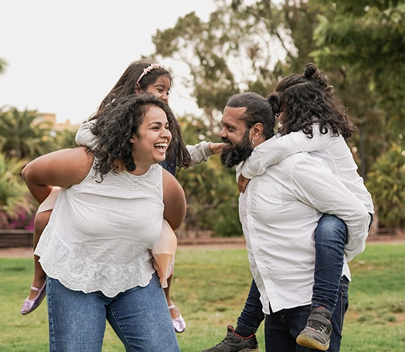 a family of 4 in the park giving piggyback rides