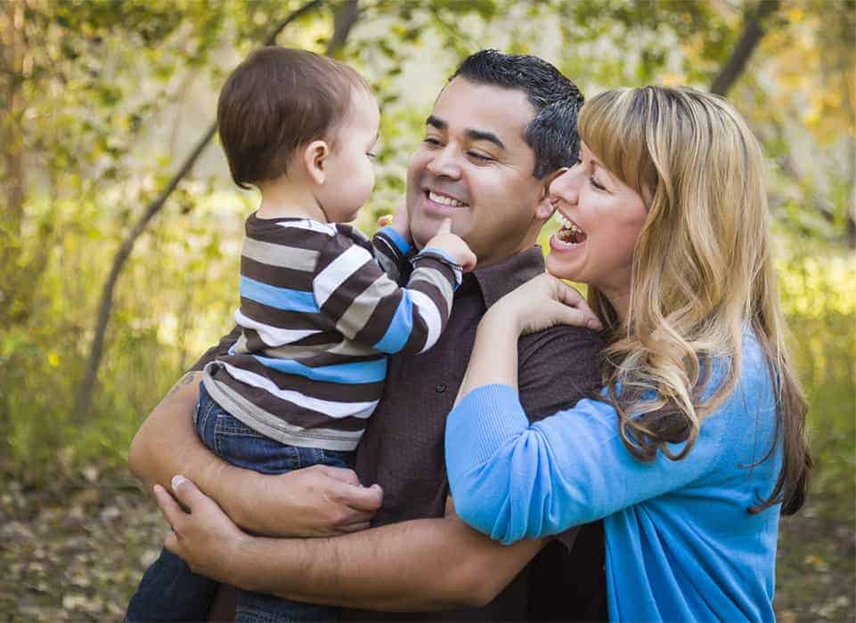 A family of three with the dad holding the kid smiling